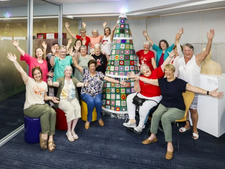 Woodvale crochet group in front of their crocheted tree